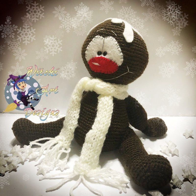 Gehäkelter brauner Lebkuchen-Amigurumi mit weißem Schal und Zuckerglasur-Akzenten vor Schneeflocken-Hintergrund.