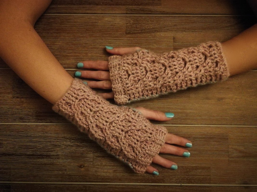 Gehäkelte fingerlose Armstulpen in Rosa mit Zopfmuster auf Händen vor Holzuntergrund