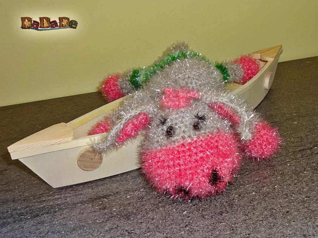Rosa-silbernes Amigurumi-Schwein aus Glitzergarn in einem Holzboot