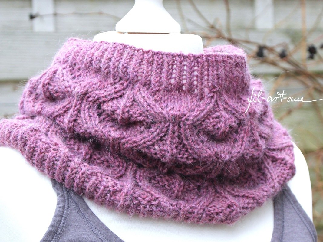 Purple cable-knit cowl with detailed cable stitchwork on a mannequin.