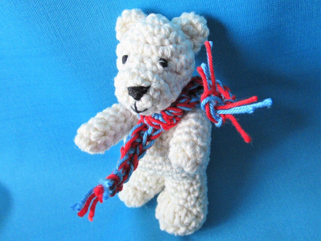 Mini gehäkelter Teddybär mit gestickten Augen und geflochtenem rot-blauem Schal