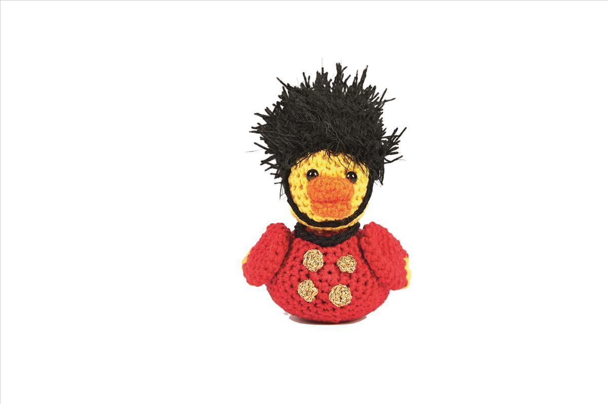 Gehäkelte Amigurumi-Ente in rotem Gardistengewand mit schwarzem Kopfschmuck