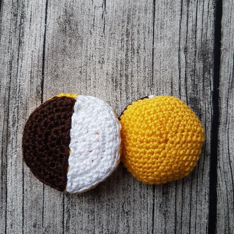 Zwei runde, gehäkelte Spiel-Lebensmittel: eines halb braun/weiß, das andere gelb