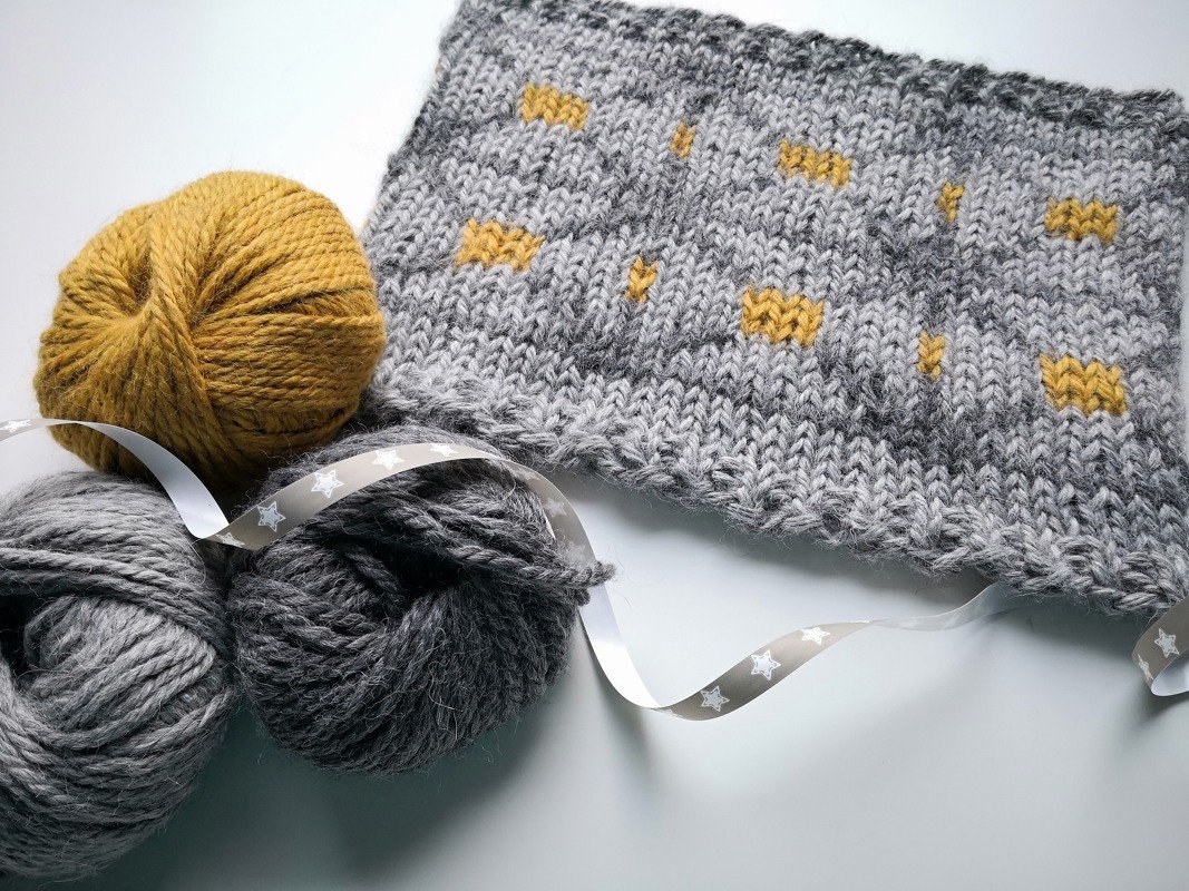 Gestricktes graues Tuch mit senfgelben Punkten, drei Wollknäueln und Sternband
