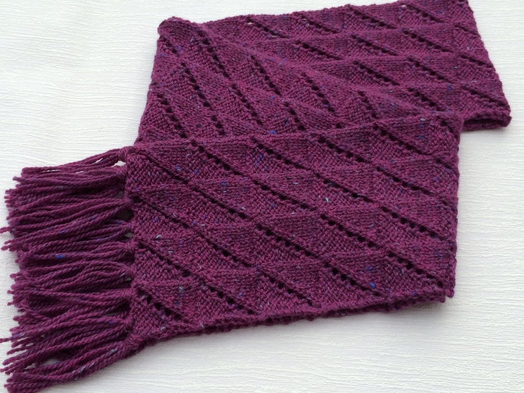 Violetter Schal mit diagonalen Lochreihen und langen Fransen auf hellem Hintergrund