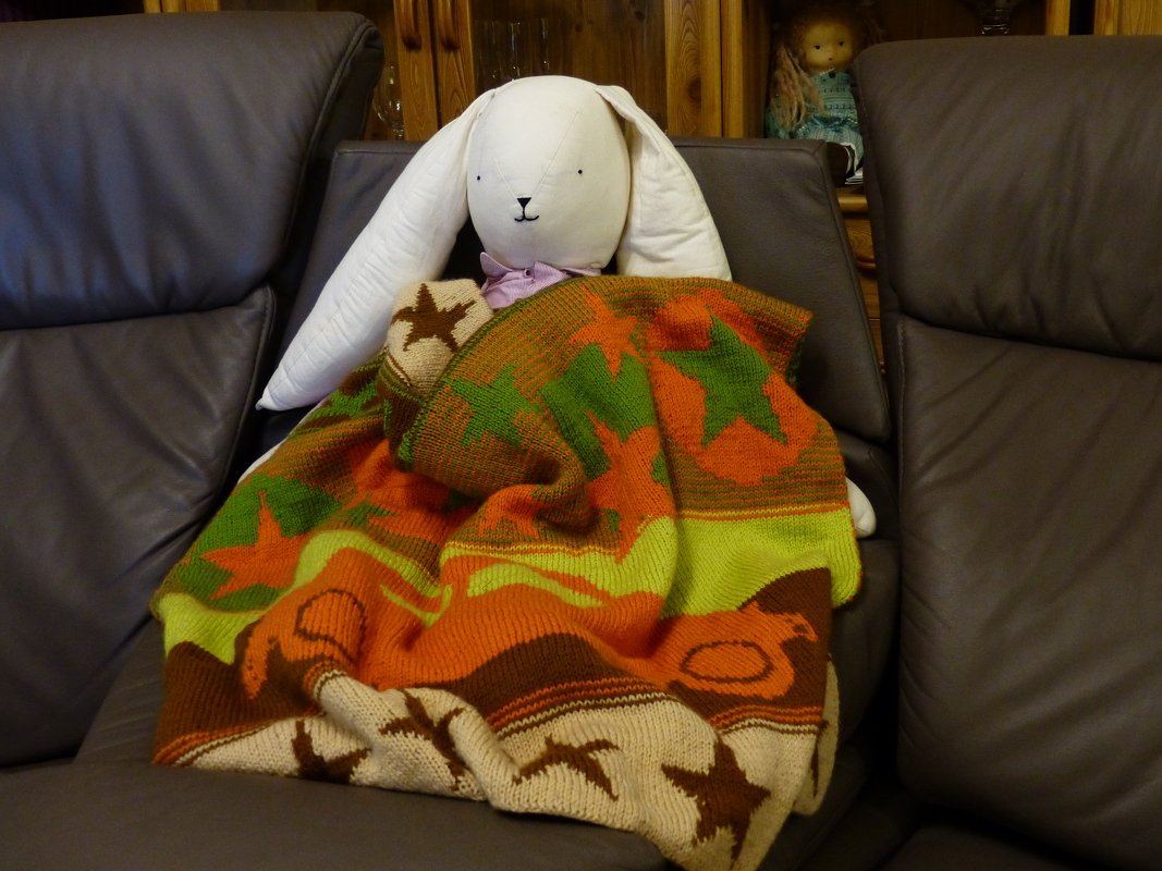 Striped baby blanket in orange, green, brown and cream with star motifs draped over a sofa with a white rabbit toy