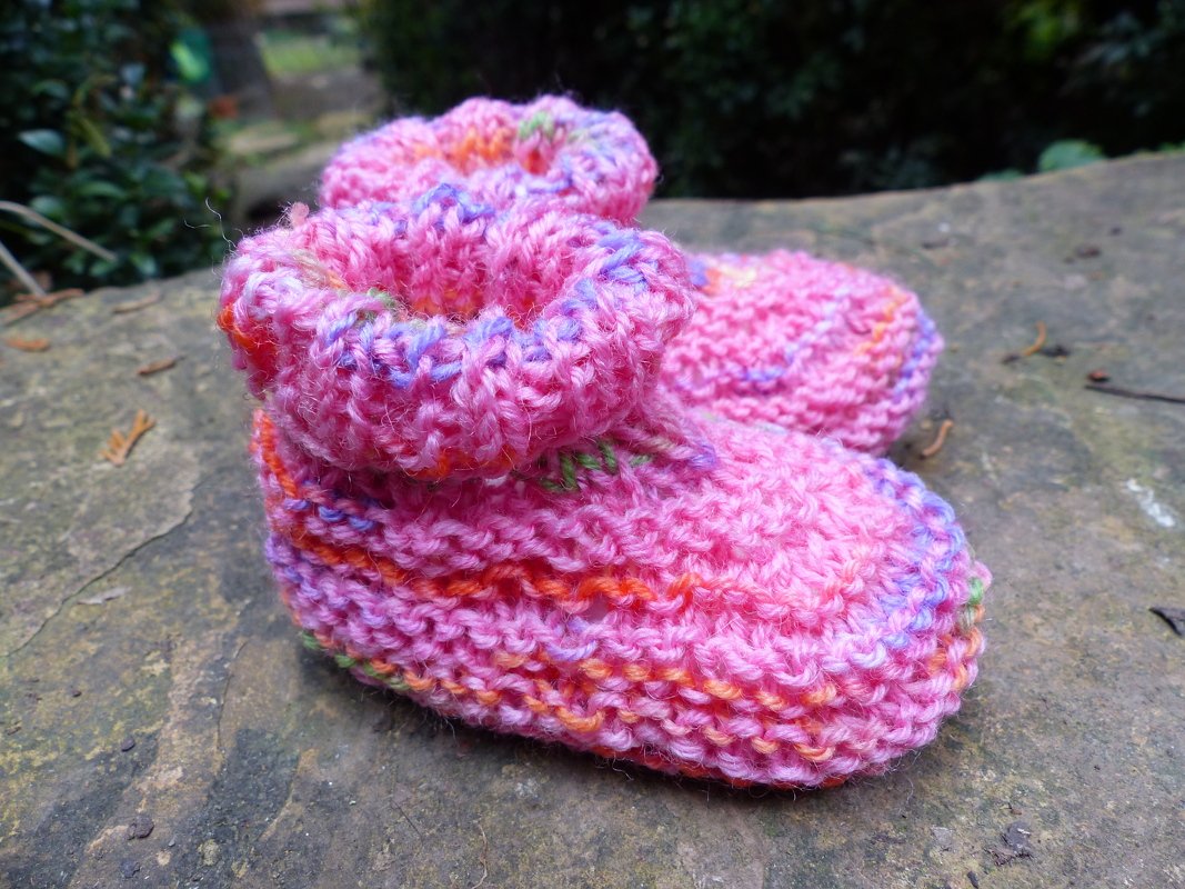 Rosafarbene gestrickte Babyschuhe mit bunten Garnakzenten auf Stein