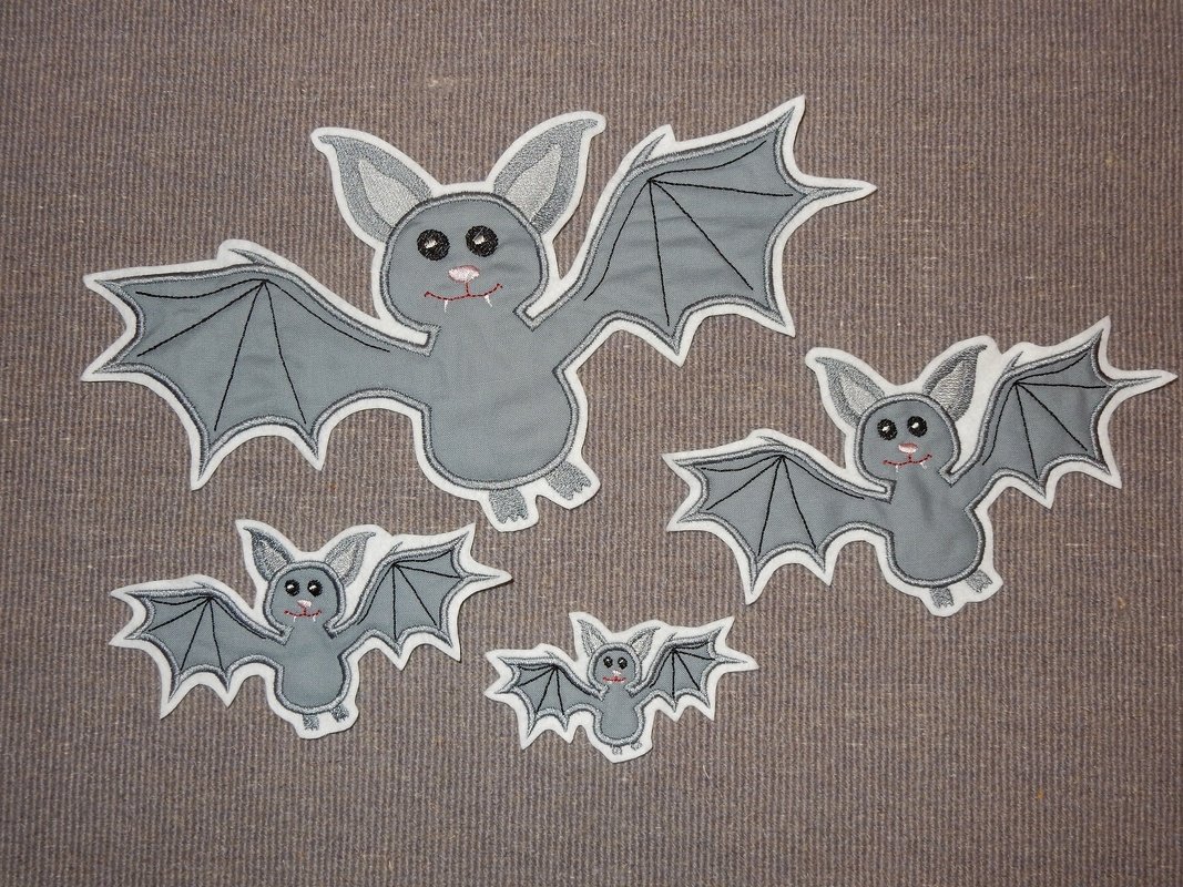Vier graue Fledermaus-Applikationen in verschiedenen Größen mit weißem Rand auf braunem Textil