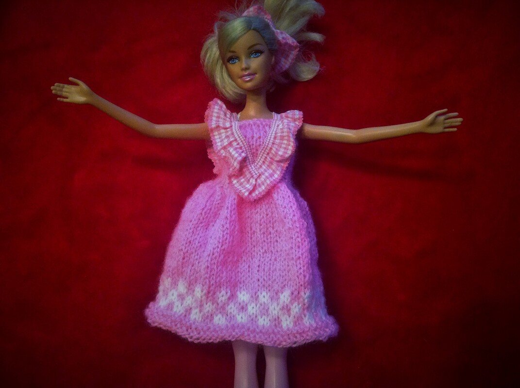 Nahaufnahme einer Puppe mit rosa gestricktem Kleid, Rüschen am Oberteil und hellem Saummuster