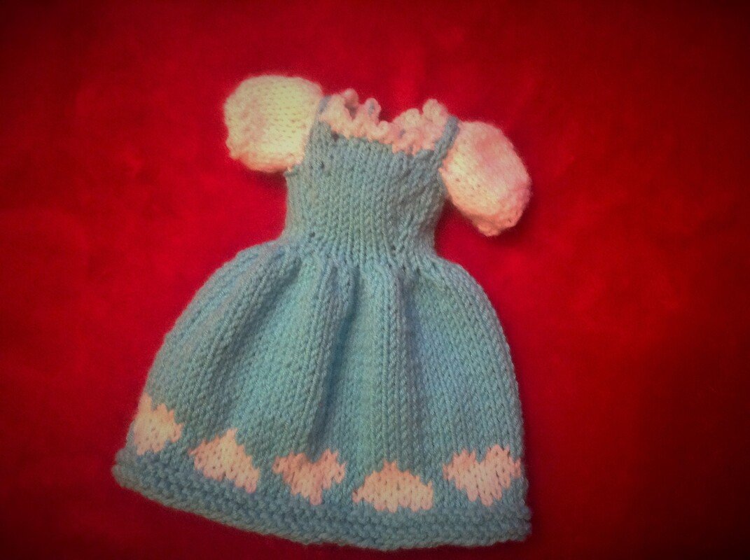 Gestricktes hellblaues Kleid mit weißen Puffärmeln und Herzmuster auf rotem Hintergrund