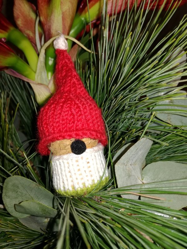 Gestrickter Wichtel mit roter Mütze und schwarzer Nase zwischen Tannenzweigen