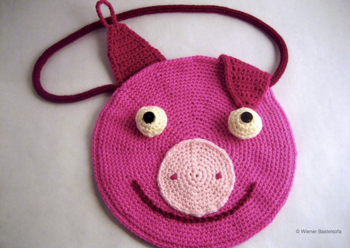 Runde rosa gehäkelte Umhängetasche in Schweineform mit hellrosa Schnauze und dunklen Knopfaugen