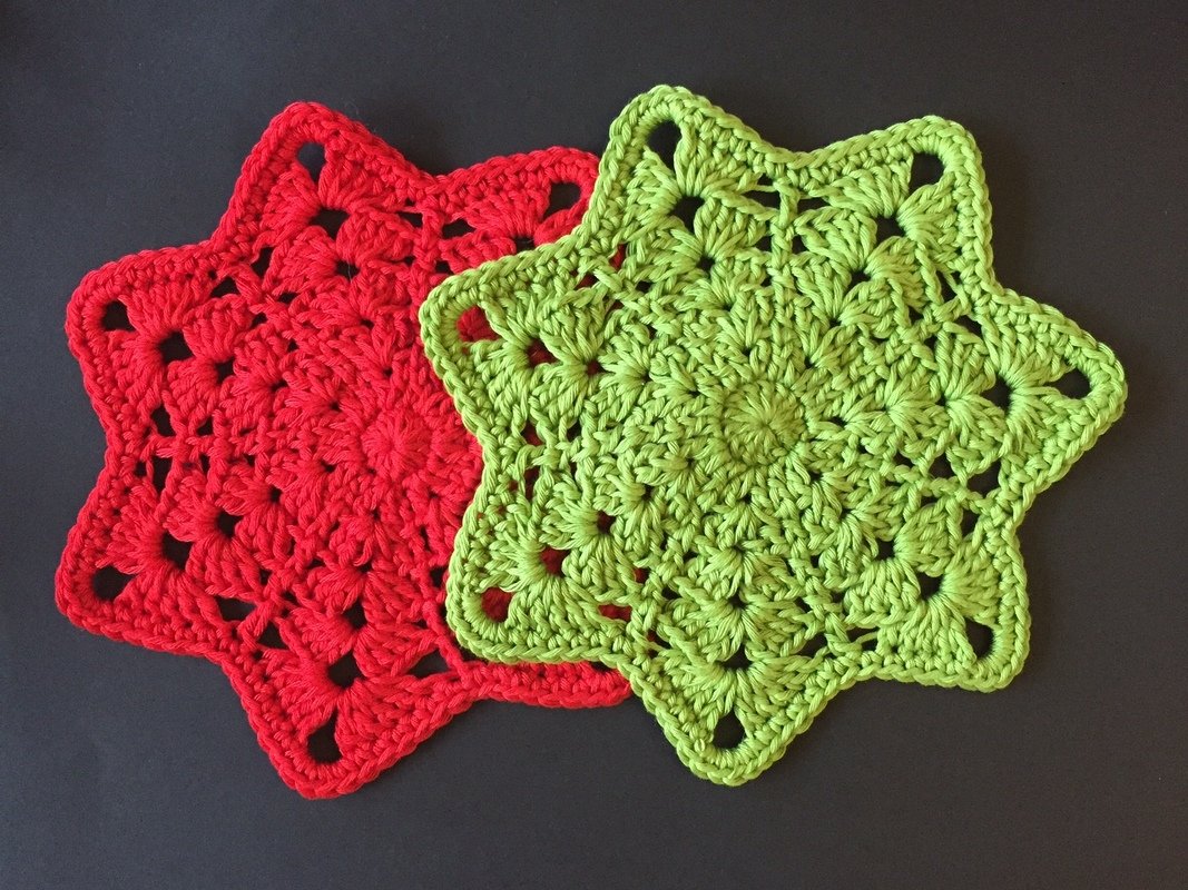 Zwei sternförmige gehäkelte Topflappen in Rot und Grün auf dunklem Hintergrund