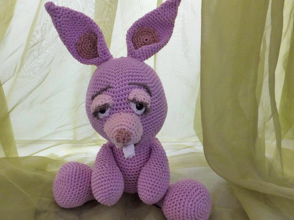 Gehäkeltes fliederfarbenes Amigurumi‑Häschen, sitzend, mit langen Ohren und sichtbaren Schneidezähnen