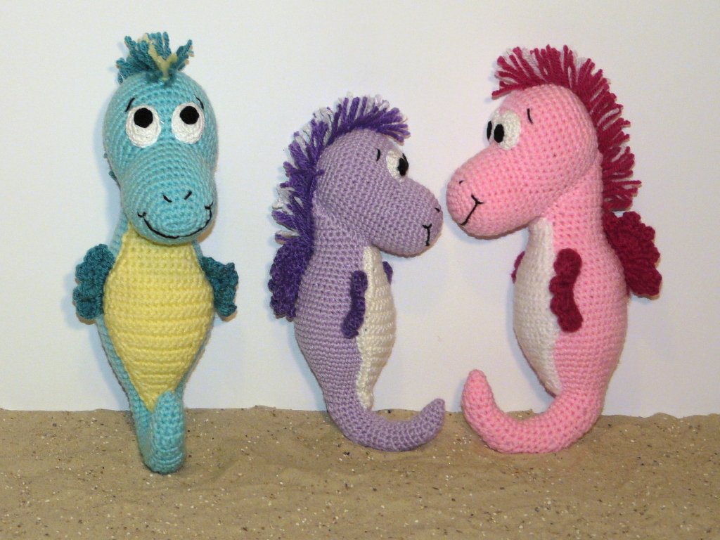 Drei gehäkelte Amigurumi-Seepferdchen in Türkis, Lila und Rosa nebeneinander