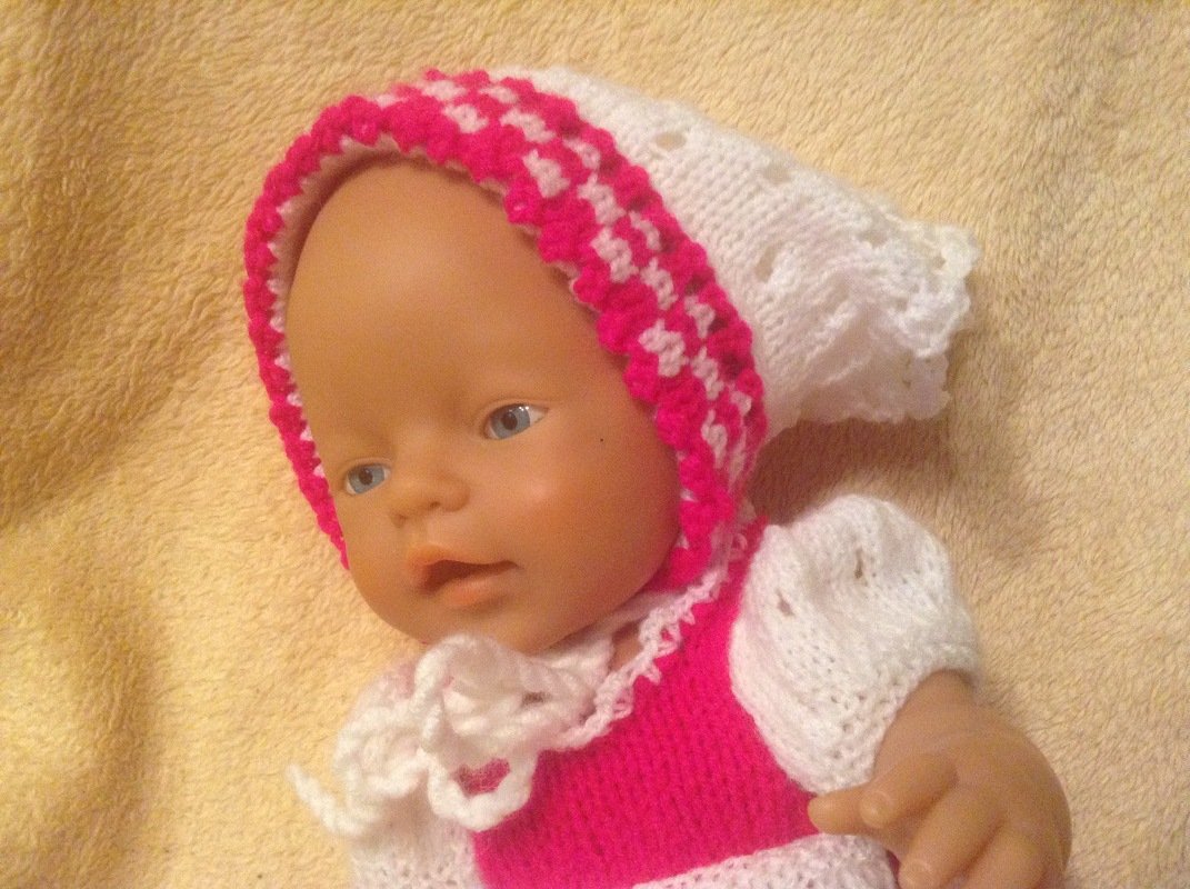 Puppe mit gestrickter pink-weißer Mütze und passendem Kleid.