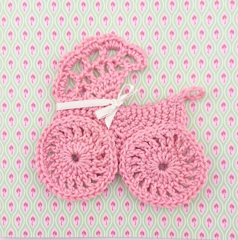 Rosa gehäkelte Kinderwagen-Applikation mit Schleife auf gemustertem Hintergrund