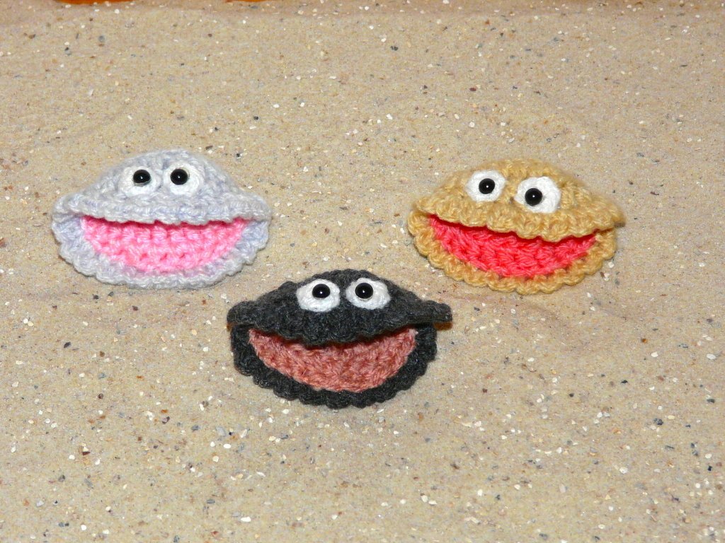 Drei gehäkelte Amigurumi-Muscheln mit Augen auf Sand