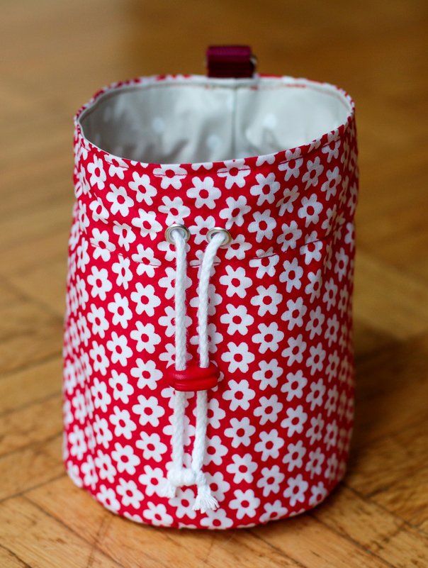 Rote Stofftasche mit weißen Blumen, Kordelzug und rotem Stopper auf Holzboden