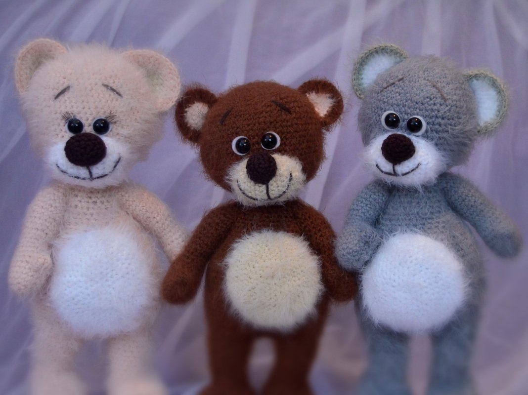 Drei gehäkelte Teddybären in Beige, Braun und Grau mit weißem Bauch und lächelnden Gesichtern.