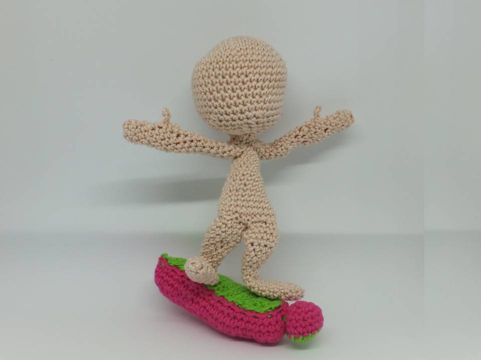 Gehäkelter Amigurumi-Puppenkörper in Beige auf pink-grünem Brett mit ausgestreckten Armen.