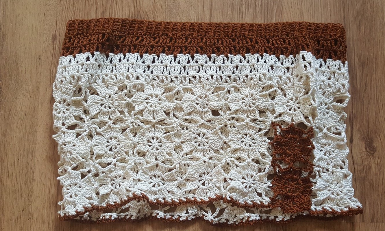 Gehäkelter Rock in Cremeweiß mit braunem Bund, liegend auf Holzboden