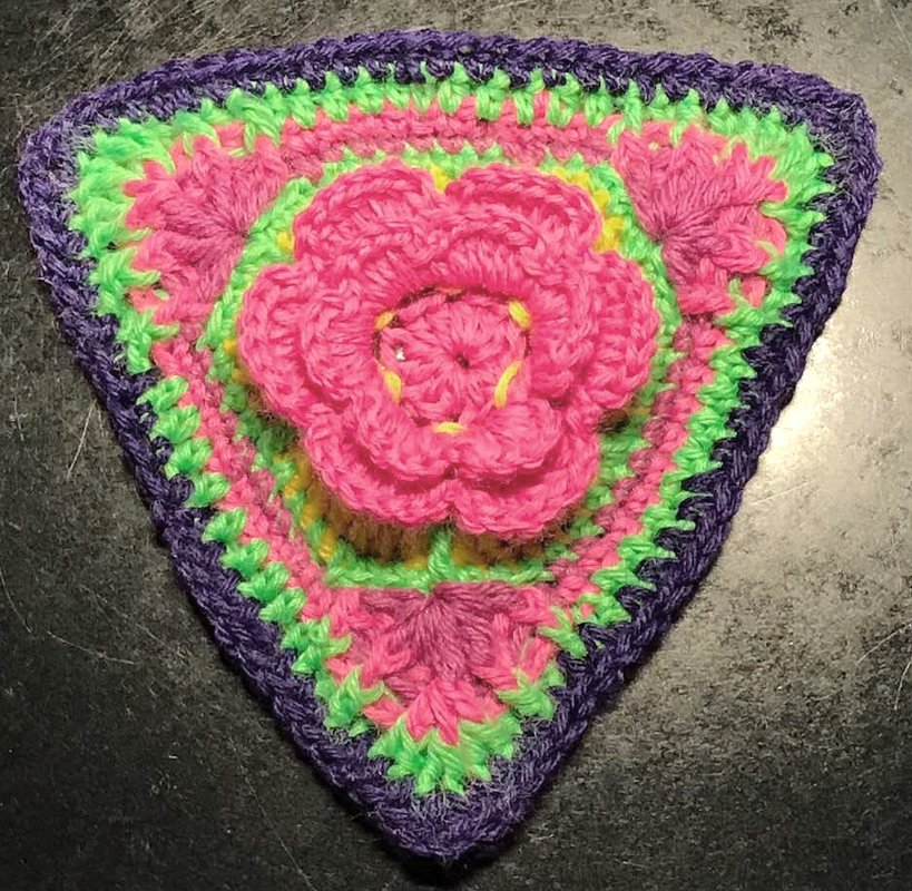 Dreieckige gehäkelte Applikation mit 3D-pinker Blüte, grünen und lila Reihen