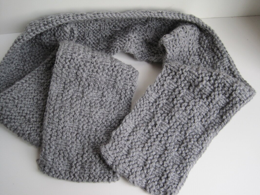 Grauer gestrickter Schal mit strukturiertem Muster auf hellem Hintergrund