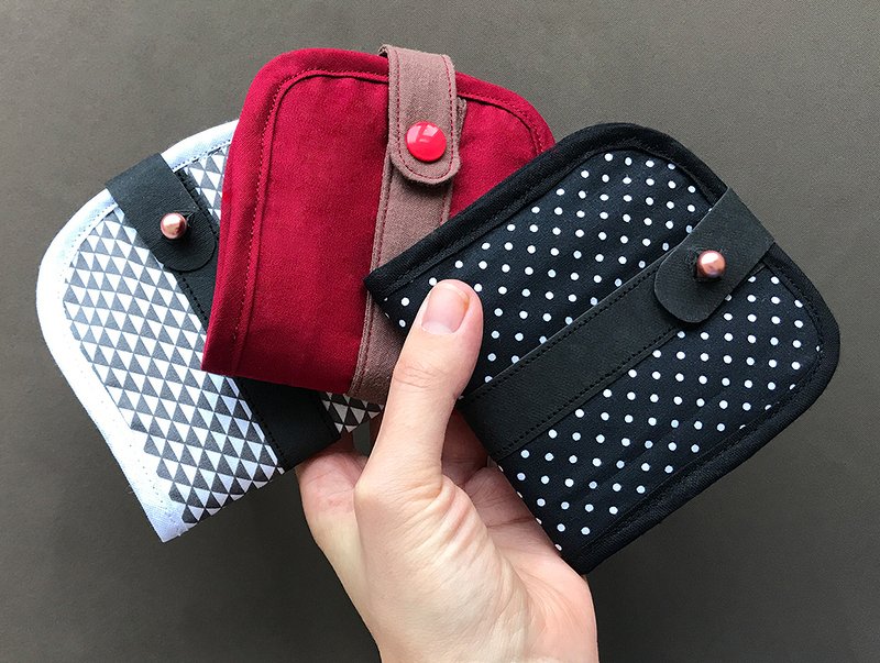 Hand hält drei kleine Stoffgeldbörsen in Rot, Schwarz mit weißen Punkten und Grau mit Dreiecksmuster, alle mit Lasche und Druckknopf