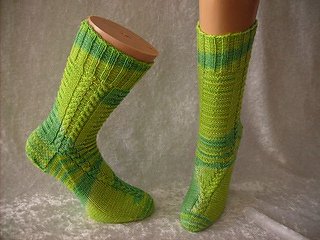 Zwei wadenhohe, grüne Stricksocken mit Zopfmuster auf einem Beinmodell