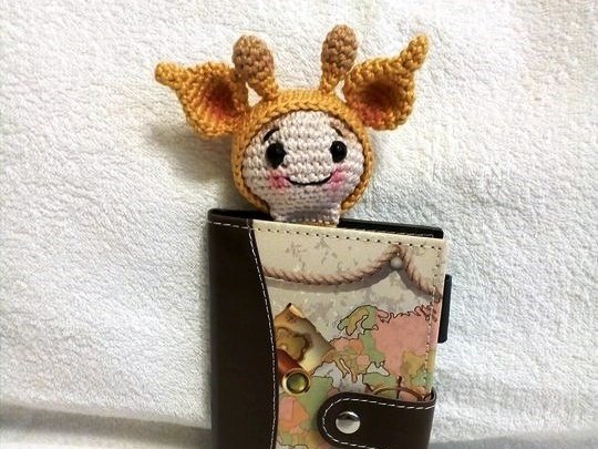 Gehäkeltes Lesezeichen in Giraffenform ragt aus einem Notizbuch mit Weltkartenmuster auf hellem Stoff