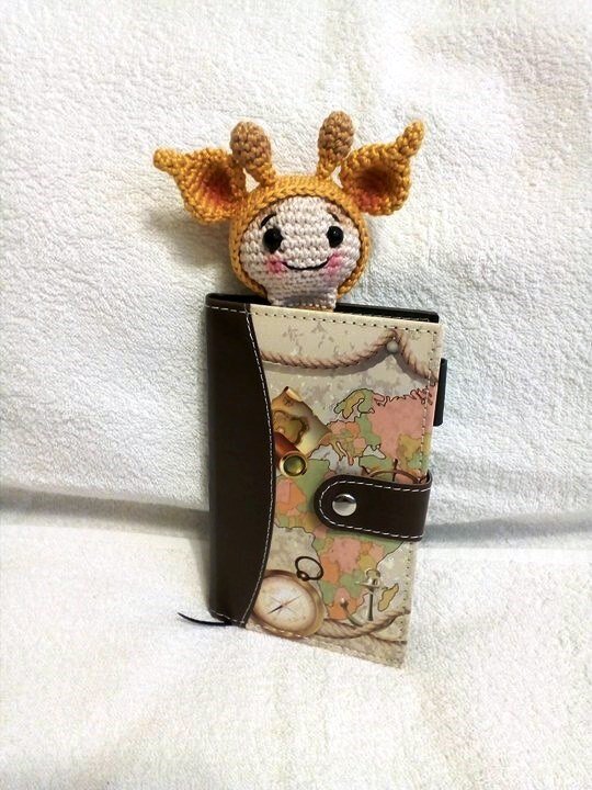 Kleines gehäkeltes Giraffenköpfchen ragt aus einem Notizbuch mit Weltkarten-Einband