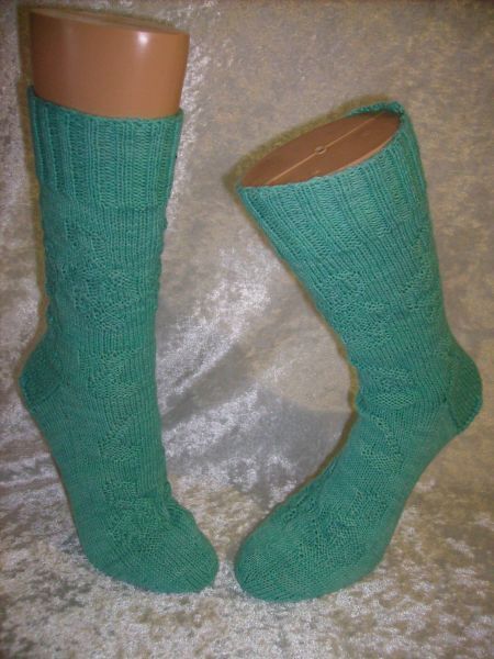 Zwei mintgrüne handgestrickte Socken mit Strukturmuster auf beigen Mannequinbeinen vor hellem Hintergrund.