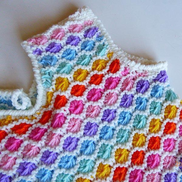 Nahaufnahme eines gestrickten Babyoberteils mit bunten Noppenmaschen und weißer Kante