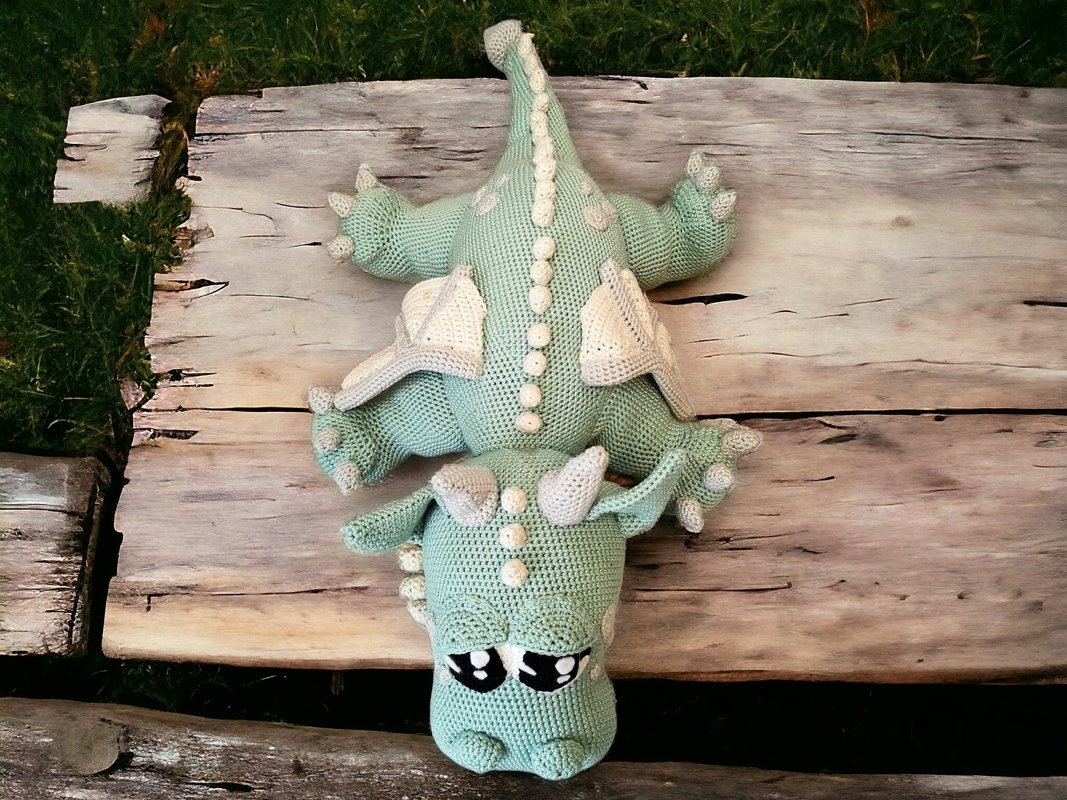 Mintgrüner, gehäkelter Amigurumi-Drache mit cremefarbenen Flügeln auf Holzbrett