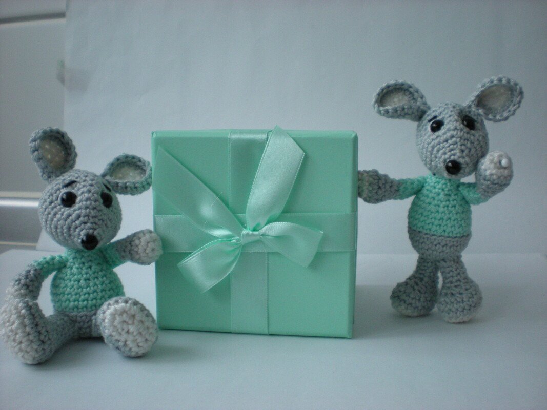 Zwei handgehäkelte Mäuse in Grau und Mintgrün neben einer mintgrünen Geschenkbox mit Satinschleife; eine sitzt, eine steht.