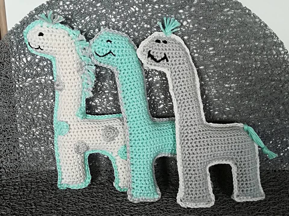 Drei gehäkelte Amigurumi-Dinosaurier in Mint, Grau und Creme nebeneinander