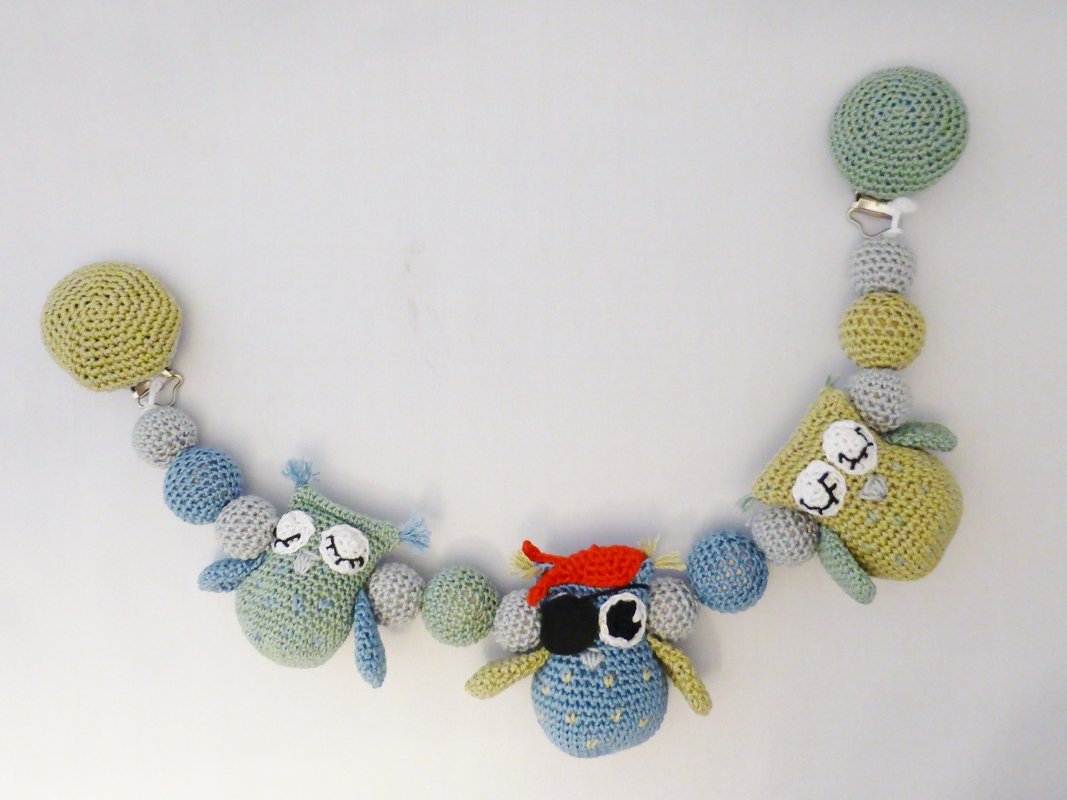 Gehäkelte Kinderwagenkette mit drei Eulen, bunten Kugeln und Befestigungsclips in Pastellfarben.