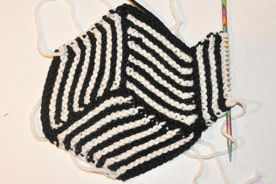 Schwarz-weißes gestricktes Zickzackmuster mit Stricknadel auf hellem Untergrund