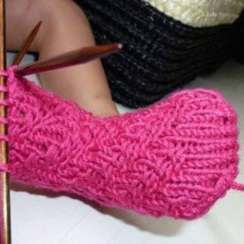 Rosa gestrickte Babysocke mit Zopfmuster auf Nadelspiel, noch in Arbeit
