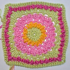 Gehäkeltes Granny Square in Grün, Pink und Orange mit floral wirkendem Kreis in der Mitte und quadratischer Umrandung.