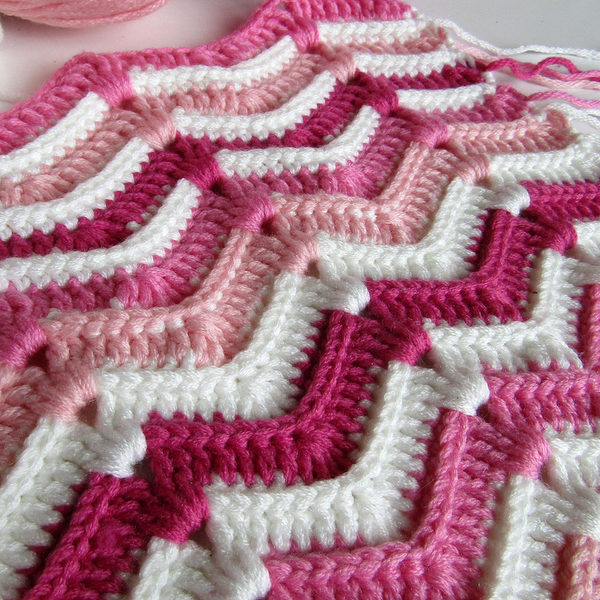 Detailaufnahme einer gehäkelten Babydecke mit Zickzackstreifen in Rosa und Weiß