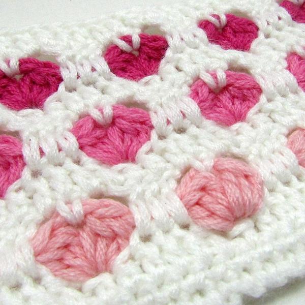 Nahaufnahme eines gehäkelten Stoffes mit rosa Herzmotiven auf weißem Grund
