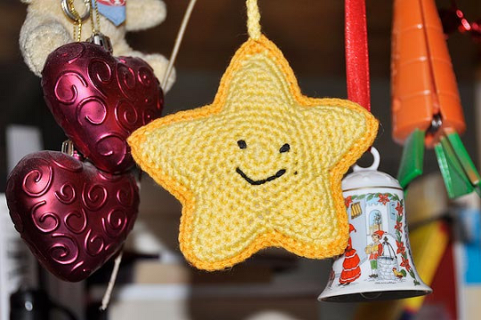 Gehäkelter gelber Stern mit Smiley, daneben rote Herzornamente und eine Glocke