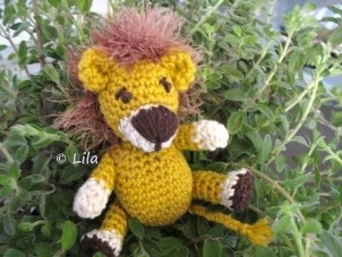 gehäkelter gelber Amigurumi-Löwe mit brauner Schnauze und flauschiger Mähne sitzt auf grünen Blättern