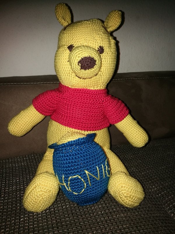 Gehäkelter gelber Amigurumi-Bär mit rotem Shirt und blauem Topf