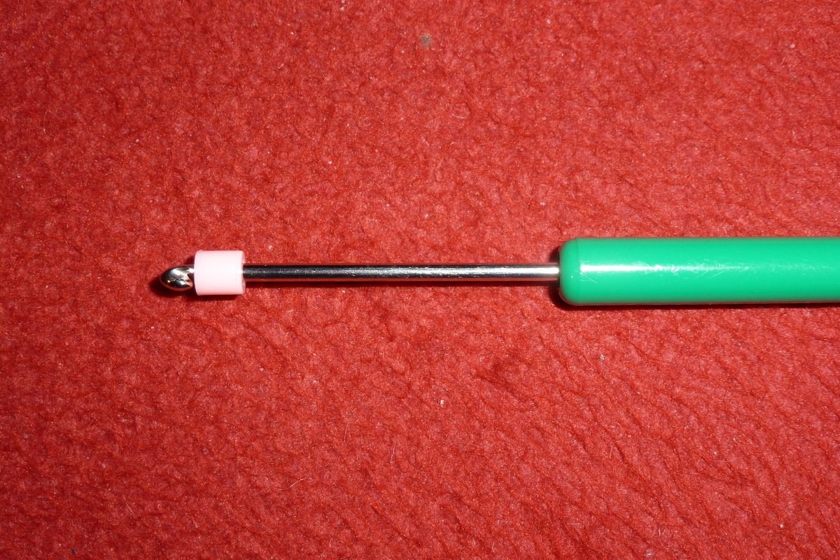 Handarbeitsnadel mit grünem Griff und rosa Stopper auf rotem Stoff