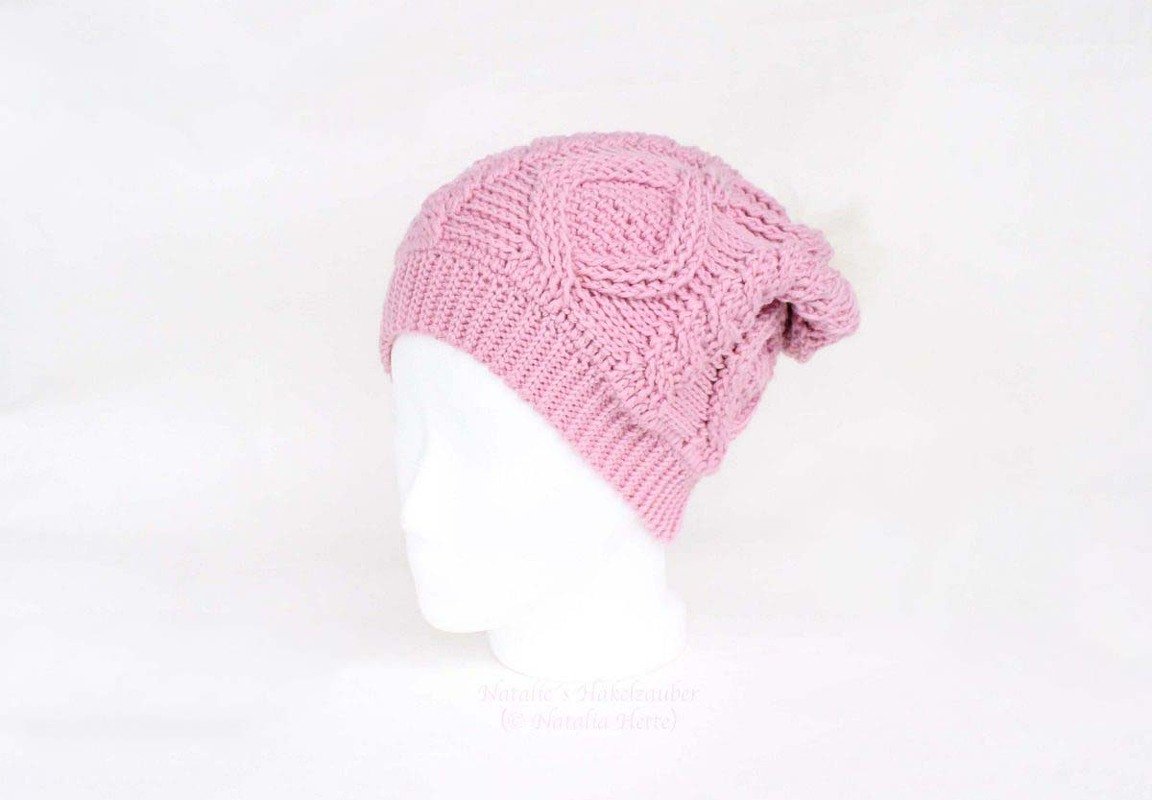 Rosafarbene gehäkelte Beanie mit Zopfmuster auf weißem Mannequinkopf.