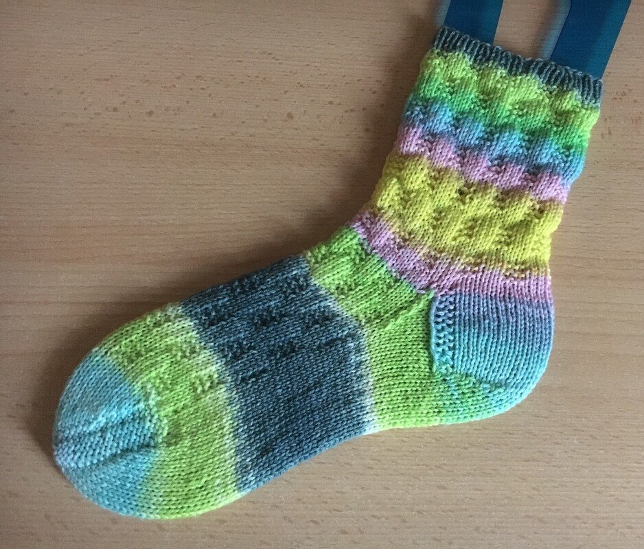 Bunte handgestrickte Socke mit horizontalem Strukturmuster auf hellem Holz