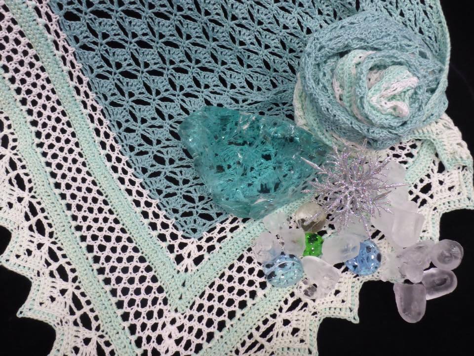 Gehäkeltes Dreieckstuch in Türkis und Weiß, Nahaufnahme mit dekorativen Glas- und Kristallobjekten